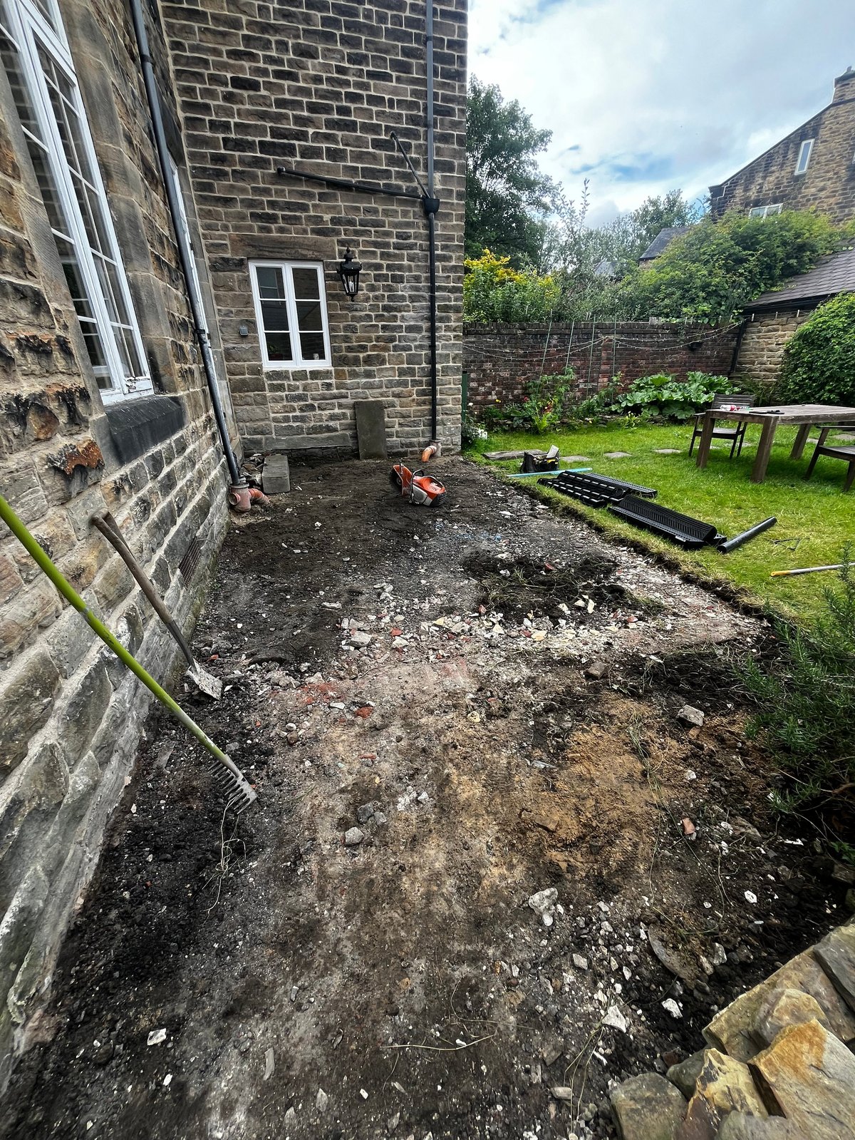 Stone cottage backyard garden under renovation with excavated ground, building materials, and grass lawn area