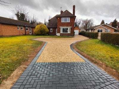 Red brick house with curved paved driveway bordered by green lawn and hedges
